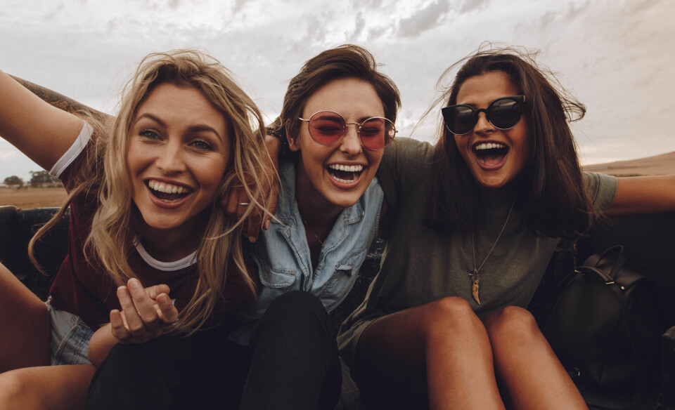 Portrait of three women sitting on back of a pickup truck and laughing. Female friends enjoying a pick truck ride in countryside road trip.