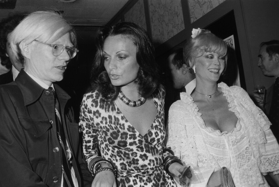 Kunstneren Andy Warhol (1928–1987), Diane von Furstenberg og skuespilleren Monique Van Vooren, hovedrolleinnehaver i Warhols film Flesh for Frankenstein, på premieren av filmen i New York City i 1974. Von Furstenberg er kledd i sitt eget design, en leopardmønstret omslagskjole.