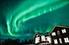 Nordlys på himmelen over en opplyst trelodge en vinternatt.