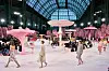 Modeller går på catwalk omgitt av store rosa og hvite soppskulpturer i en hall med glasstak.