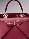 Burgunderrød Dior-håndveske med sløyfe og gullringer i nærbilde