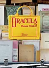 Gul Dior-veske med Dracula-trykk plassert mellom gamle bøker