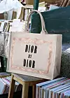 Beige Dior-handlenett med påskriften «Dior by Dior» foran stabler med bøker.