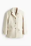 Lys kremfarget blazer med knapper og lommer mot hvit bakgrunn.