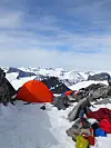 Oransje telt i snøen på fjelltopp med utsikt over snødekte fjell.