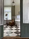 Klassisk baderom med frittstående badekar og sjakkrutete gulv sett gjennom døråpning