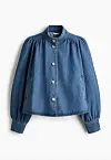 Blå denimjakke med runde knapper og vide ermer vist mot hvit bakgrunn.