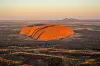 Luftfoto av Uluru som lyser oransje i solnedgang omgitt av flatt, tørt landskap.