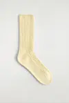 En enkelt smørgul, ribbestrikket sokk liggende mot lys bakgrunn.