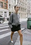 Person går over et gatehjørne iført kort jakke og miniskjørt i bymiljø.