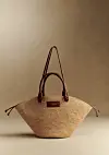 Stråveske med brune skinnhåndtak fotografert mot nøytral bakgrunn.