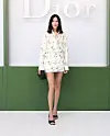 Kvinne i lys, mønstrete minikjole står foran hvit Dior-logo og grønn vegg.