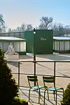 Grønn Dior-paviljong i en park med metallgjerde og grønne stoler i forgrunnen.