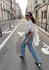 Kvinne går over en rolig bygate i hvit bluse, jeans og høye hæler.