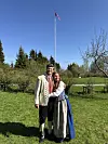 Smilende par i bunad står tett sammen på grønn plen med flaggstang i bakgrunnen.
