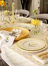 Påskebord med gule blomster, dekorative tallerkener, linservietter og vinglass.