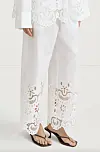 Hvite vide bukser med broderte hullmønstre og sandaler mot lys bakgrunn.
