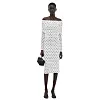 Person i hvit, skulderløs prikkekjole står mot hvit bakgrunn med liten veske.