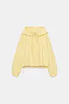 Lys gul hettejakke med snøring og vide ermer mot hvit bakgrunn.