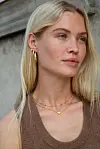 Kvinne utendørs med enkle gullsmykker og ermeløs topp i nøytral farge.