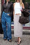To kvinner står utendørs; den ene har blå jeans og leopardmønstrede slingbacks, den andre hvit topp, blondeskjørt og svarte sandaler.