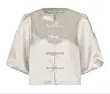 Beige satengbluse med korte puffermer og fire dekorative knapper mot hvit bakgrunn.