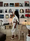 Et lyst rom med hvit bildevegg, innrammede bilder, skap, skrivebord, stoler og lamper.