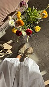 Beige sneakers ved en fargerik blomsterbukett på et gulv i sollys.