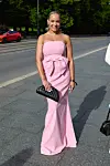 En person står på fortauet i en lang rosa kjole og holder en svart clutch.