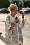 En kvinne i hvit, dekorert kjole holder en mobiltelefon og en liten clutch utendørs.