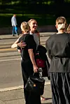 Tre personer står og snakker på fortauet ved en vei, med en bil og en gående person i bakgrunnen.