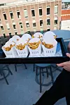 En hånd bærer et brett med fire hvite pappesker med ELLE-logo og pommes frites.