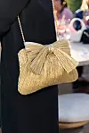 Nærbilde av en gullfarget clutch med sløyfe og lenkestropp som henger mot en mørk kjole.