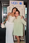 To kvinner poserer foran en UGG-stand med logo og dekorert bakgrunn.