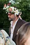En mann med solbriller og blomsterkrans står utendørs blant andre gjester.