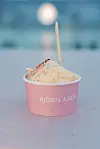 Rosa beger med Björn Axén-logo fylt med iskrem og en vaffelpinne står på et bord.