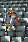 Kvinne sitter alene i en tom stadiontribune omgitt av grønne seter.