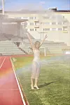Person med armene løftet på en fotballbane mens vannspray fyller stadion.