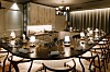 Et moderne restaurantrom med stort bord, små bordlamper og dekkede kuverter i varme beige og brune toner.