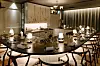 Et moderne restaurantrom med stort bord, små bordlamper og dekkede kuverter i varme beige og brune toner.