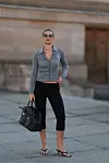 Kvinne står utendørs med svart veske, grå cardigan, svarte leggings, solbriller og svarte sandaler.