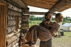 Charles og Caroline Ingalls står ved en tømmerhytte med landskap og telt i bakgrunnen.