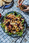 En stor skål med salat, fiken, granateple og nøtter på et bord med rutemønster.