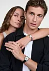 To personer poserer tett sammen mot lys bakgrunn, begge med Daniel Wellington-klokker synlige.