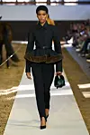 Modell på catwalken til Stella McCartney i svart peplumjakke med belte og faux fur-detalj.
