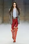 En modell på catwalken til Chloé i rutete blazer, lys skjorte, røde bukser og høye støvletter.
