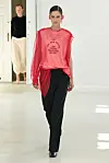 Modell på catwalken i en rød, transparent topp og svarte bukser under Anne Sofie Madsen SS27.