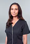 En kvinne står foran en lys grå bakgrunn og ser rett mot kamera i en mørk topp med hvit kant.