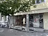 Butikkfasade med store vinduer, markise og klær utstilt ved fortauet.