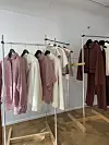 Klesstativer med hengende klær i rosa, beige og brunrøde farger i et lyst rom.